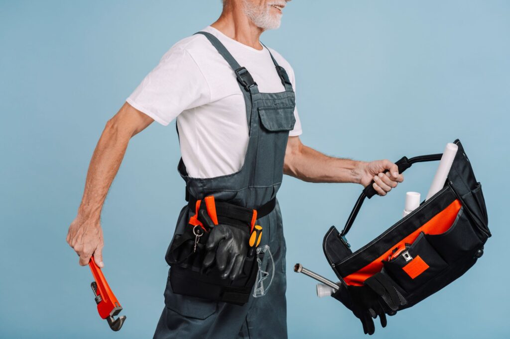 senior repairman holding pipe wrench and tool bag